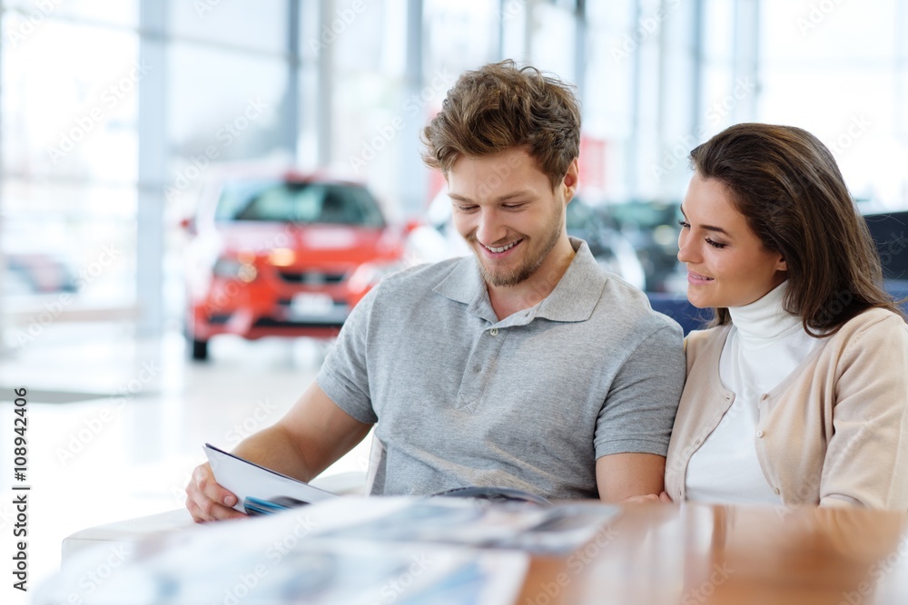 Obraz premium Beautiful young couple looking a new car at the dealership showroom.