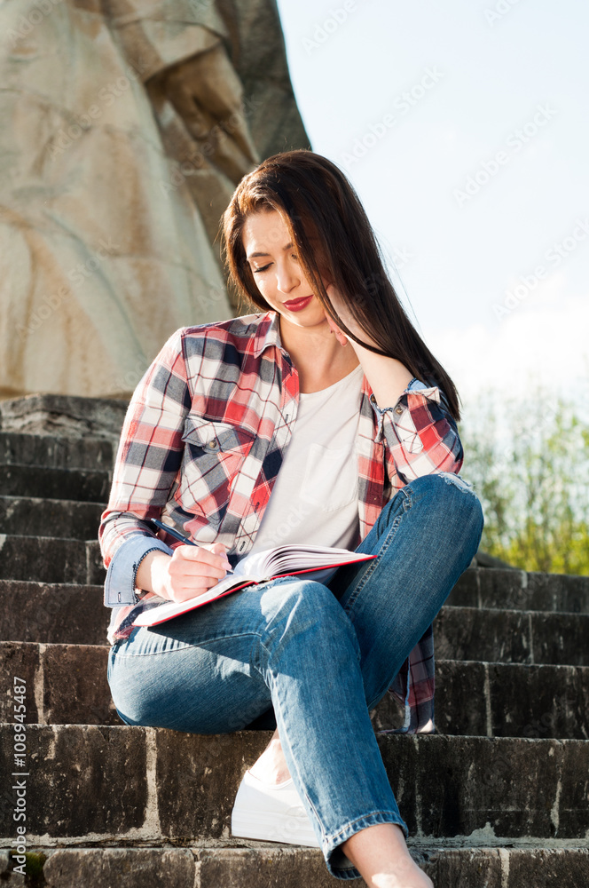 Lovely woman writing on notebook and sitting on stone stairs Lovely woman writing on notebook and sitting on stone stairs