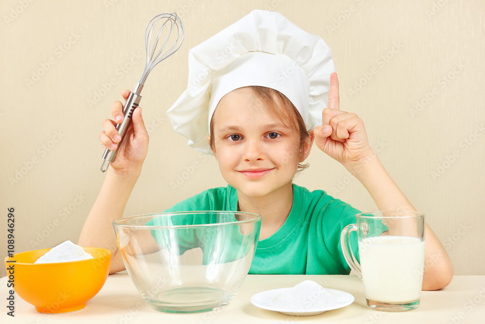 Little boy in chef hat at the table with ingredients is going to cook a cake Little boy in chef hat at the table with ingredients is going to cook a cake