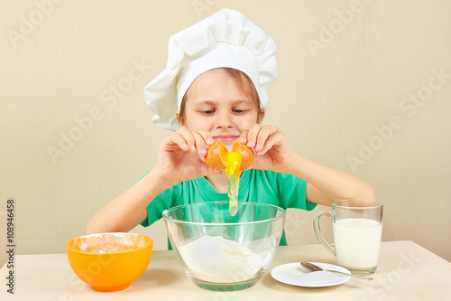 Little boy in chef hat pours egg for baking the cake