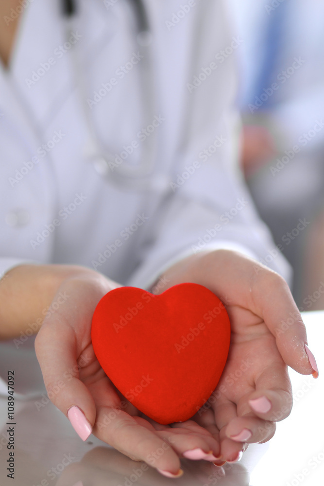 Female doctor with stethoscope holding heart. Patients couple sitting in the background Female doctor with stethoscope holding heart. Patients couple sitting in the background