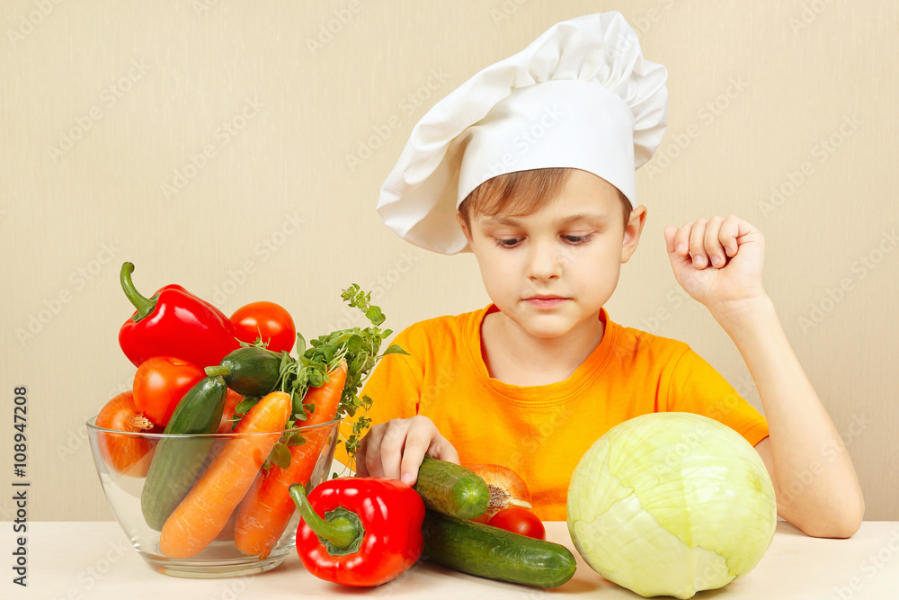 Little chef chooses vegetables for salad at the table Little chef chooses vegetables for salad at the table