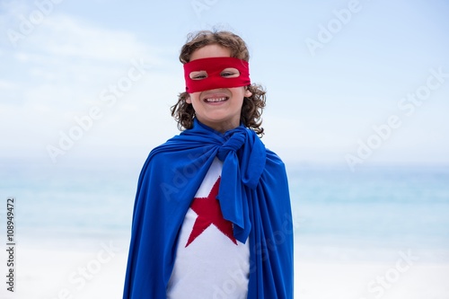 Boy wearing superhero costume standing at beach 