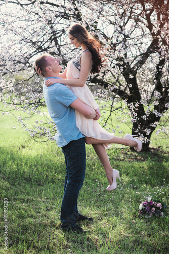 A man holding a happy woman in her arms in blossom spring garden,lifestyle,relationships photo