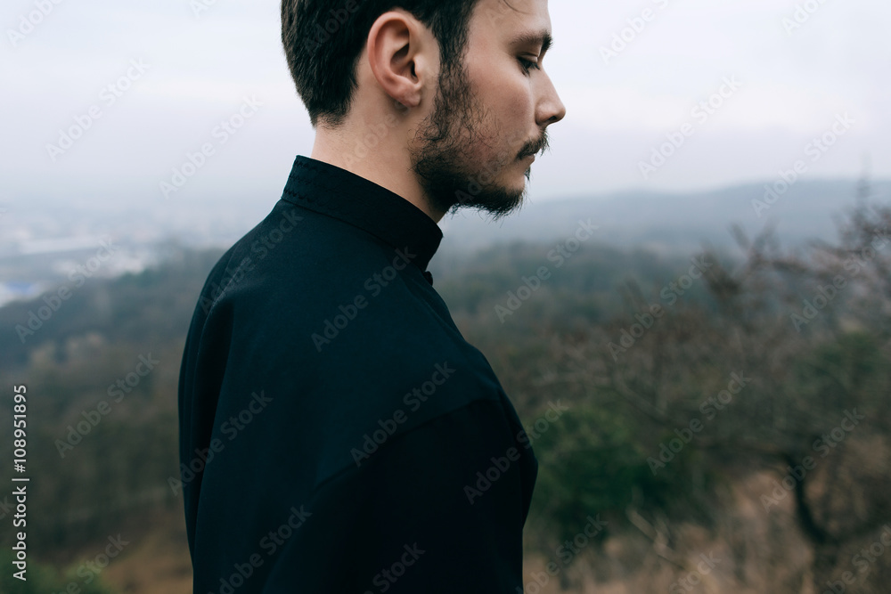 Portrait of handsome catholic bearded man priest or pastor posing outdoors in mountains Portrait of handsome catholic bearded man priest or pastor posing outdoors in mountains