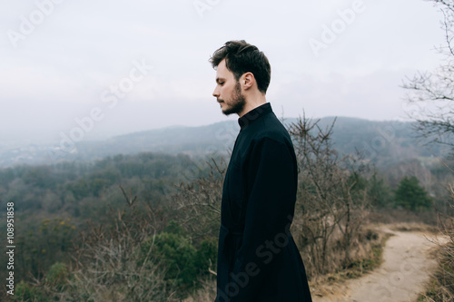 Portrait of handsome catholic bearded man priest or pastor posing outdoors in mountains