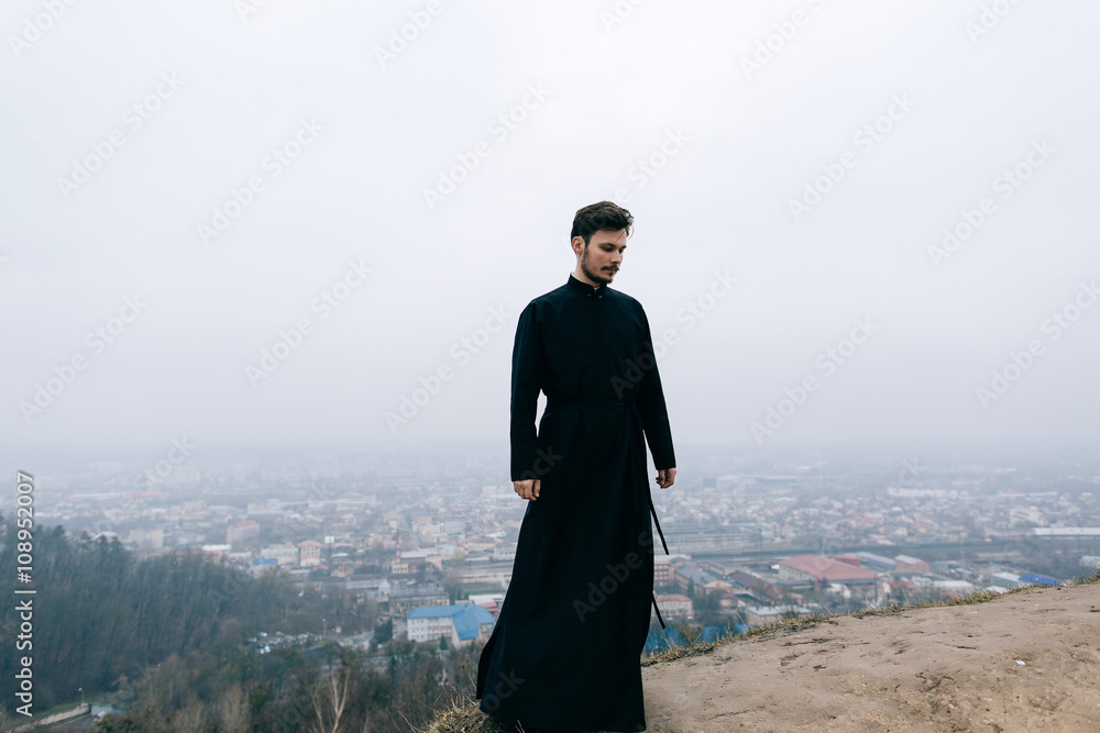 Priest bearded man raised his hands up on the hill above the town. Pastor posing outdoors in mountains Priest bearded man raised his hands up on the hill above the town. Pastor posing outdoors in mountains