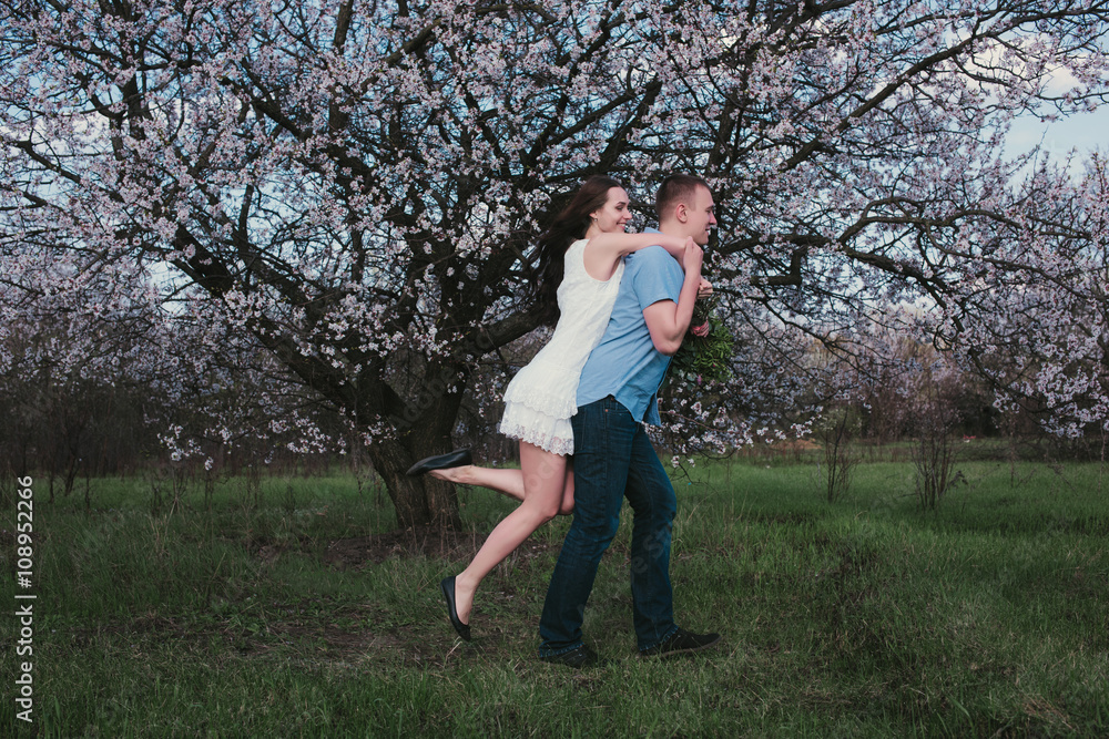 Beautiful young couple dancing and having fun on blue sky background in bloom garden,lifestyle