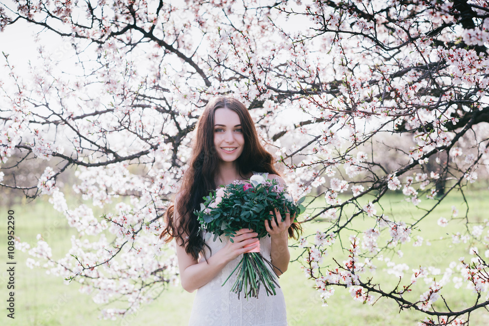 Woman in blooming trees. Woman with wedding bouquet in hands. Beautiful posing in a blooming apple garden.Spring mood. Young woman outdoors Woman in blooming trees. Woman with wedding bouquet in hands. Beautiful posing in a blooming apple garden.Spring mood. Young woman outdoors