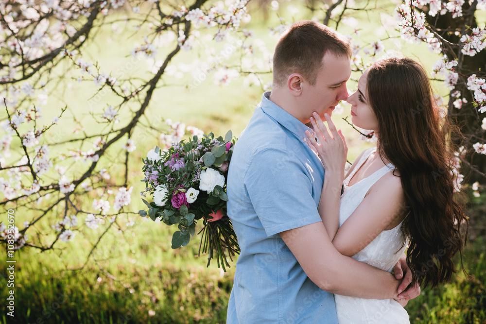 Young couple in love outdoor.Stunning sensual outdoor portrait of young stylish fashion couple posing in spring near blossom tree Young couple in love outdoor.Stunning sensual outdoor portrait of young stylish fashion couple posing in spring near blossom tree