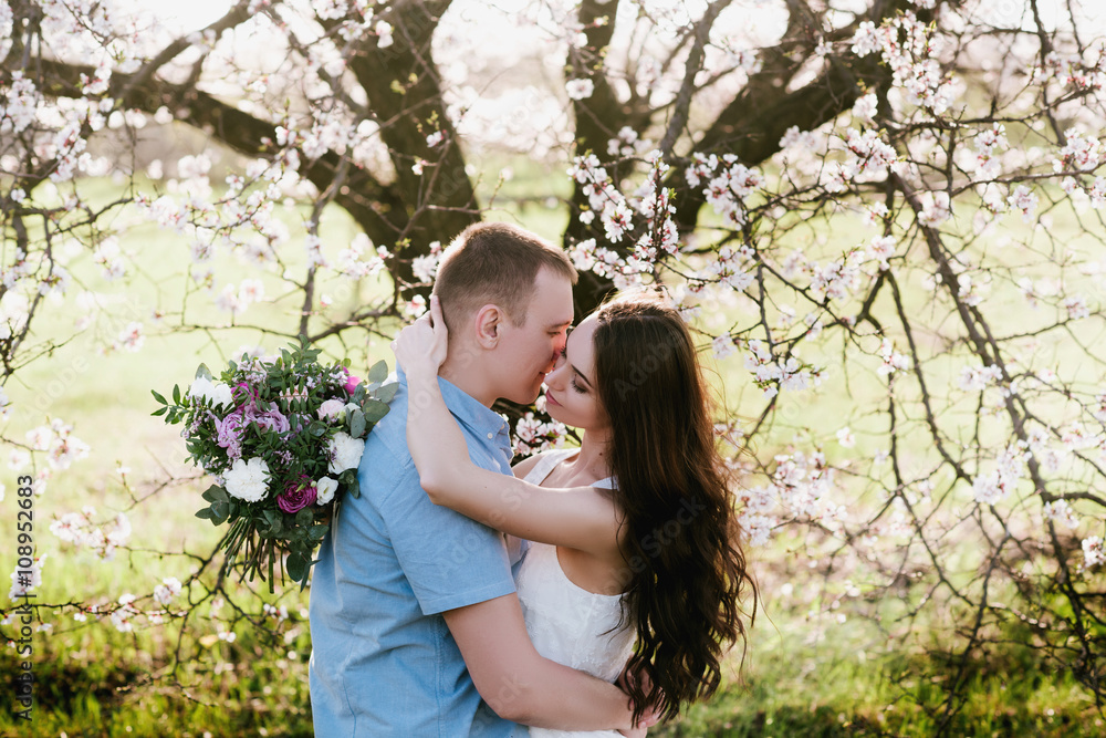 Young couple in love outdoor.Stunning sensual outdoor portrait of young stylish fashion couple posing in spring near blossom tree Young couple in love outdoor.Stunning sensual outdoor portrait of young stylish fashion couple posing in spring near blossom tree