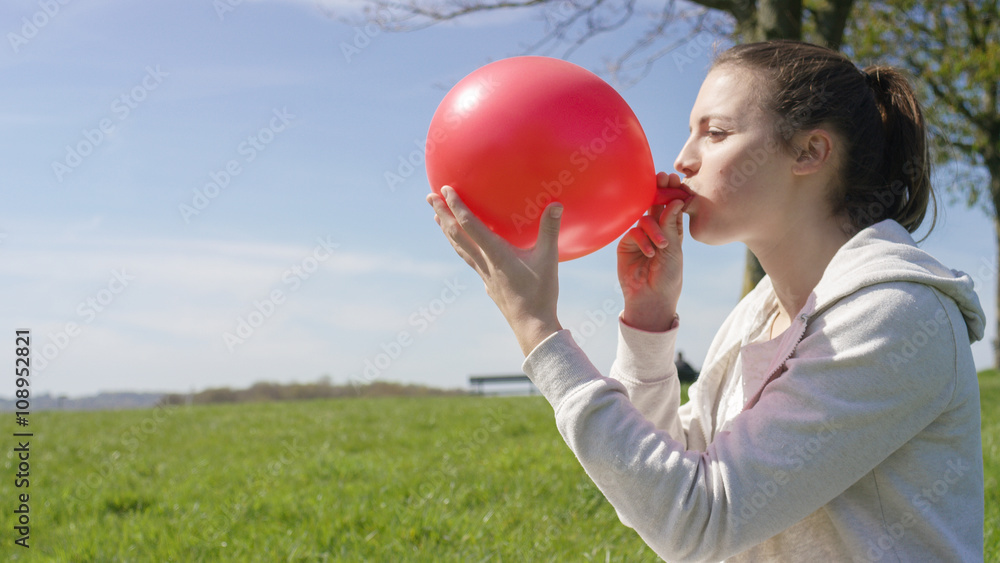 Female blowing up a red balloon Female blowing up a red balloon