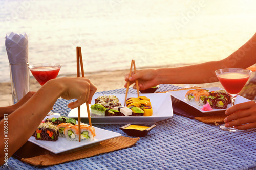 Obraz na płótnie The dinner with japanese sushi roll set at the beach on the sunset w salonie