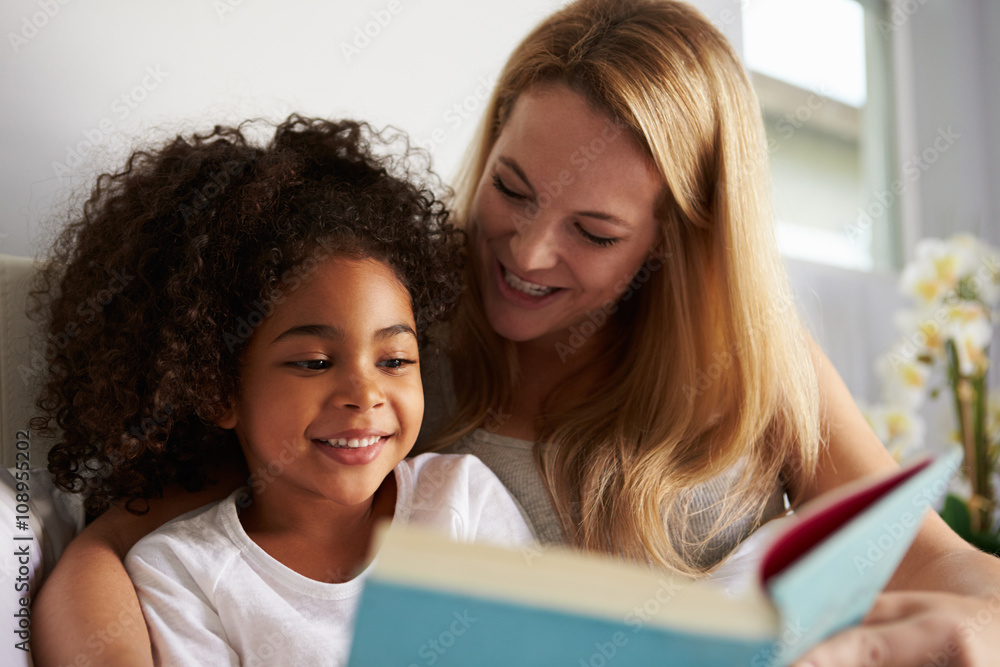 Caucasian mum and smiling black daughter read in bed, close-up Caucasian mum and smiling black daughter read in bed, close-up