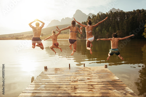 Photographie Young friends jumping into lake from a jetty