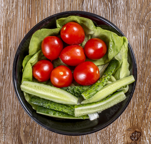 Tomato, cucumber and lettuce in a plate on wooden background