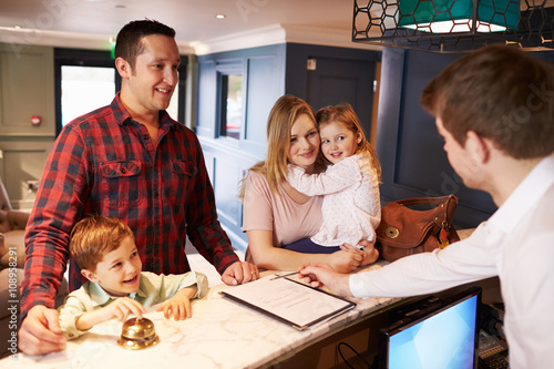 Family Checking In At Hotel Reception Desk
