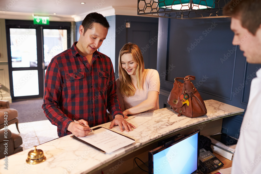 Couple Checking In At Hotel Reception Desk