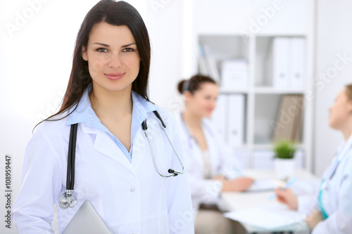 Brunette female doctor on the background of colleagues talking to each other in hospital