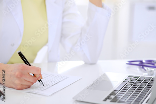 Close-up of a female doctor filling  out application form , sitting at the table in the hospital