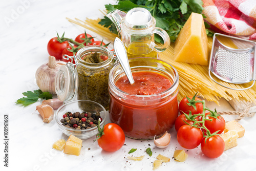 tomato sauce, pesto and ingredients for pasta on a white table