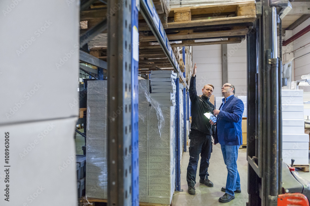 Manager and warehouseman discussing logistics in storage Manager and warehouseman discussing logistics in storage