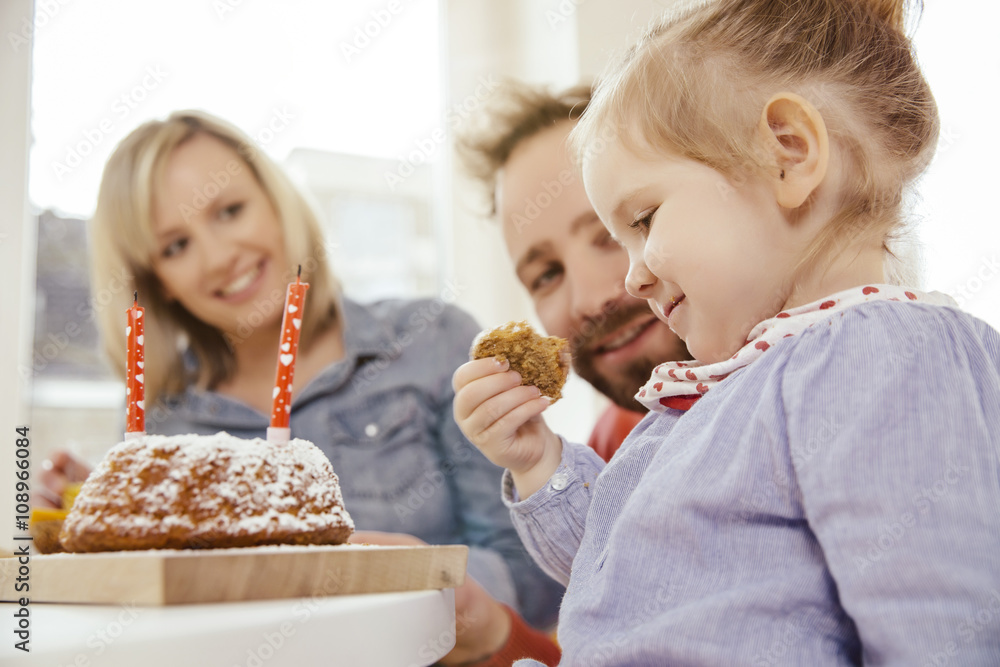 Little girl having a piece of her carrot birthday cake while parents watching Little girl having a piece of her carrot birthday cake while parents watching