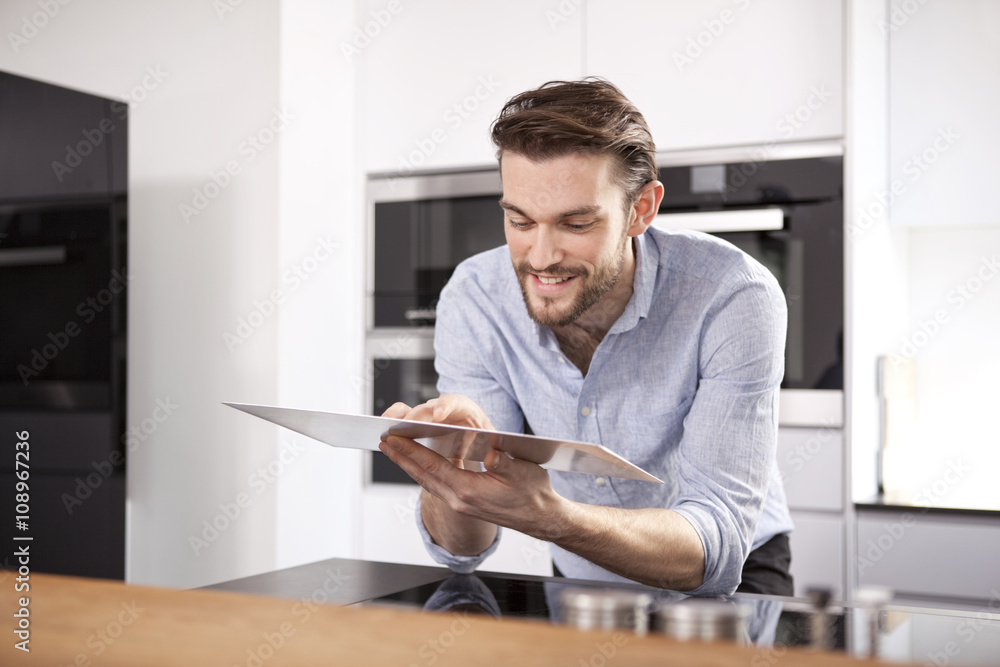 Portrait of smiling young man using digital tablet in his kitchen Portrait of smiling young man using digital tablet in his kitchen
