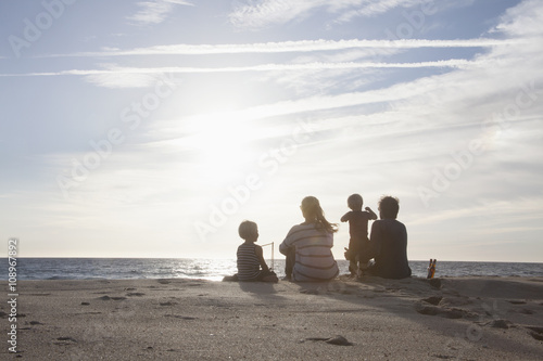 Back view of family with two kids sitting on the beach at twilight photo