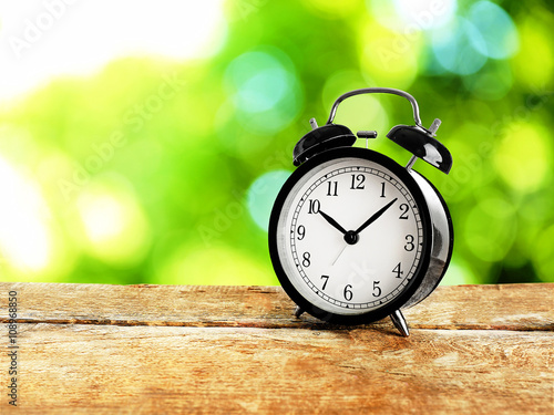 Alarm clock on wooden table on bright background