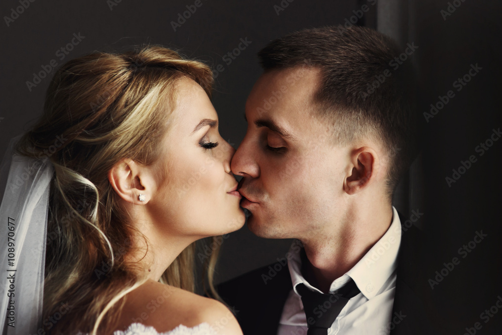 Romantic happy couple, bride & groom kissing near window closeup Romantic happy couple, bride & groom kissing near window closeup