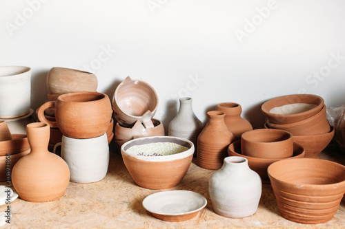 Antique clay crockery set  on white background. Many handmade ceramics objects on wooden shelf. Brown clay crockery in pottery workshop. 