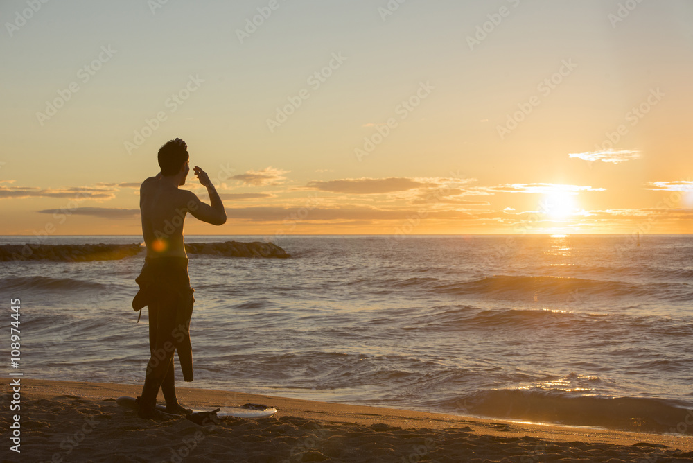 Back view of surfer standing on the beach watching sunrise Back view of surfer standing on the beach watching sunrise