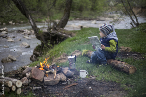 Teenager sitting near a fire in camping and watching map.