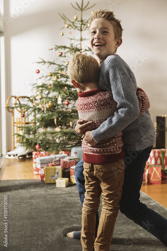 Two brothers waiting in front of Christmas tree looking at presents
