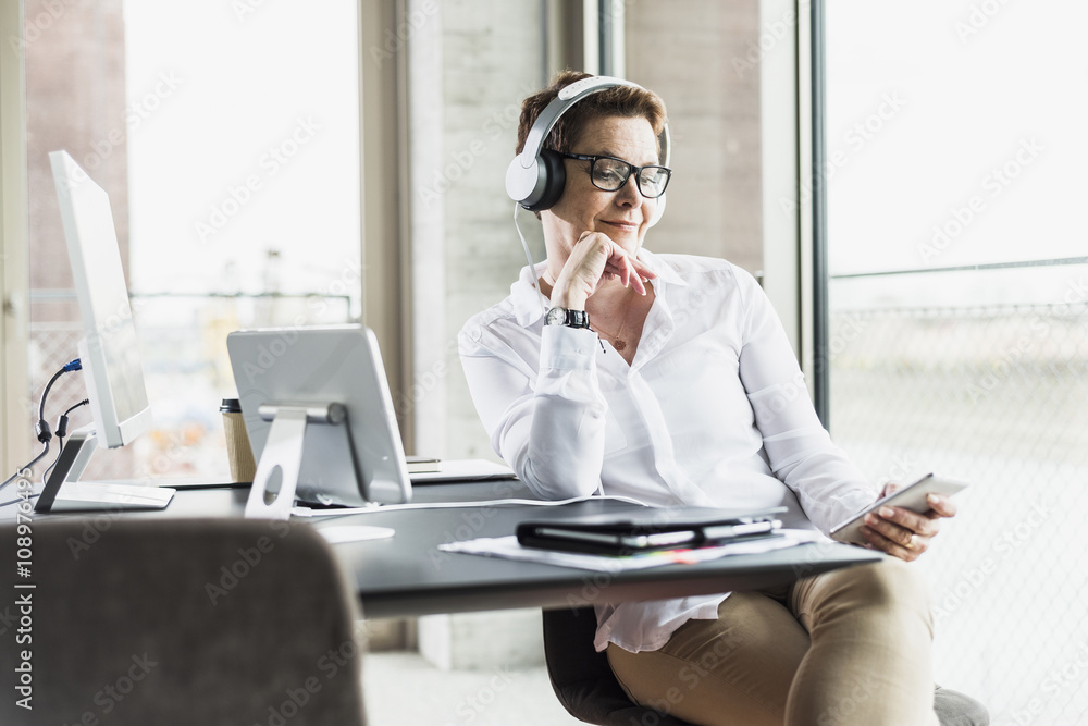 Businesswoman with cell phone and headphones in office Businesswoman with cell phone and headphones in office