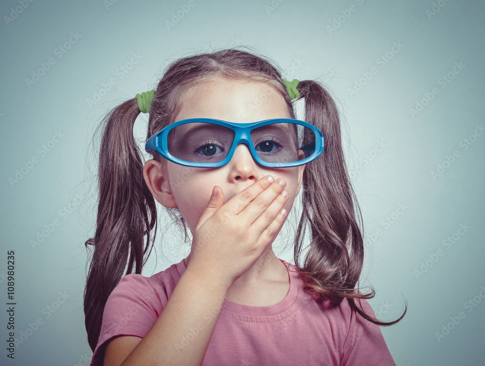 excited cute little girl with 3d glasses closing her mouth by her hand excited cute little girl with 3d glasses closing her mouth by her hand