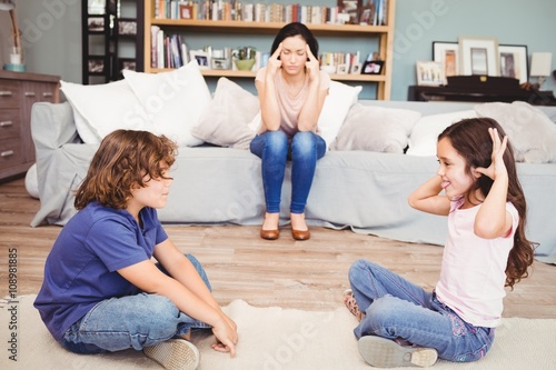 Children playing while tensed mother sitting on sofa