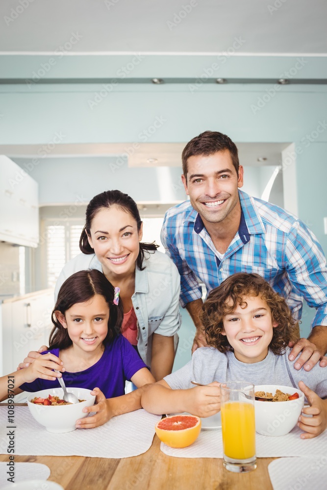 Portrait of cheerful man and woman with children having breakfast at home