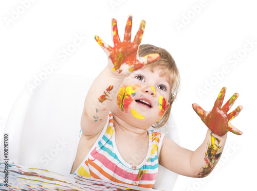 Child with hands in paint using paintbrush and colors for the first time. 