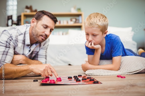 Close-up of father and son playing checker game while lying on floor at home
