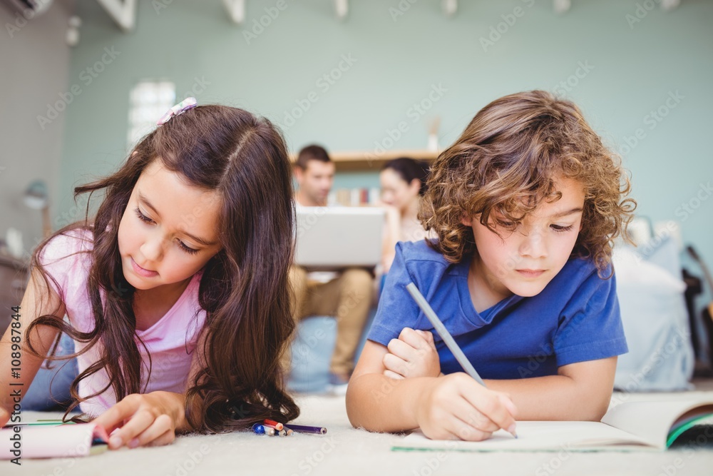 Close-up of children studying while parents in background at home Close-up of children studying while parents in background at home