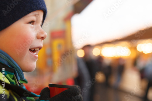 Close-up of a 5 years old boy in a winter hat and gloves drinking tea outdoors and watching city lights. Drinking hot chocolate after ice skating.