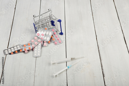 Shopping cart with pills and syringes on white wooden desk