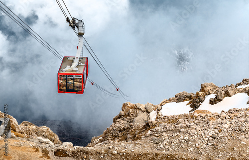 Cabin of ropeway in mountains among clouds in the sky.