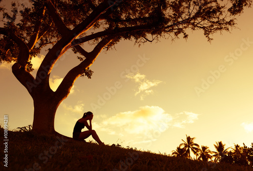 Fototapeta Sad young woman sitting outdoors under a tree.