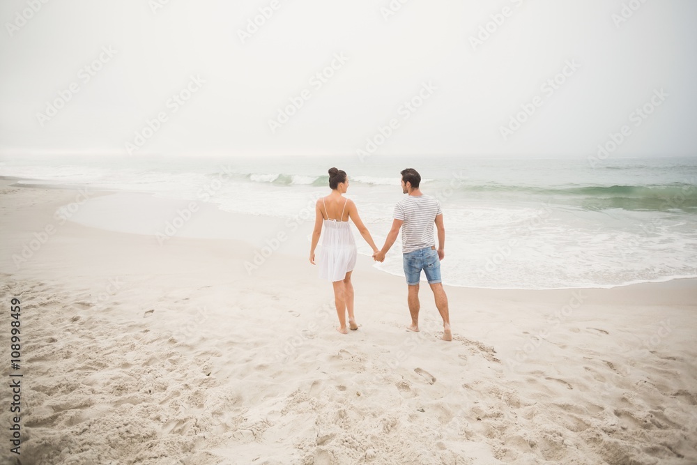 Rear view of couple holding hands and walking on the beach