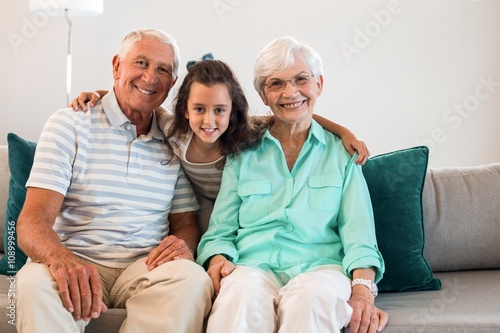 Portrait of grandmother and grand father with their granddaughter sitting on sofa in living room