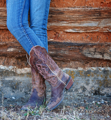Western style image of cowgirl's legs in jeans and boots on deserted wall background