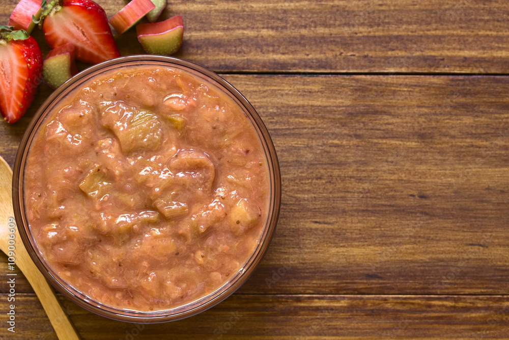 Homemade rhubarb and strawberry chutney in glass bowl, photographed overhead on dark wood with natural light Homemade rhubarb and strawberry chutney in glass bowl, photographed overhead on dark wood with natural light
